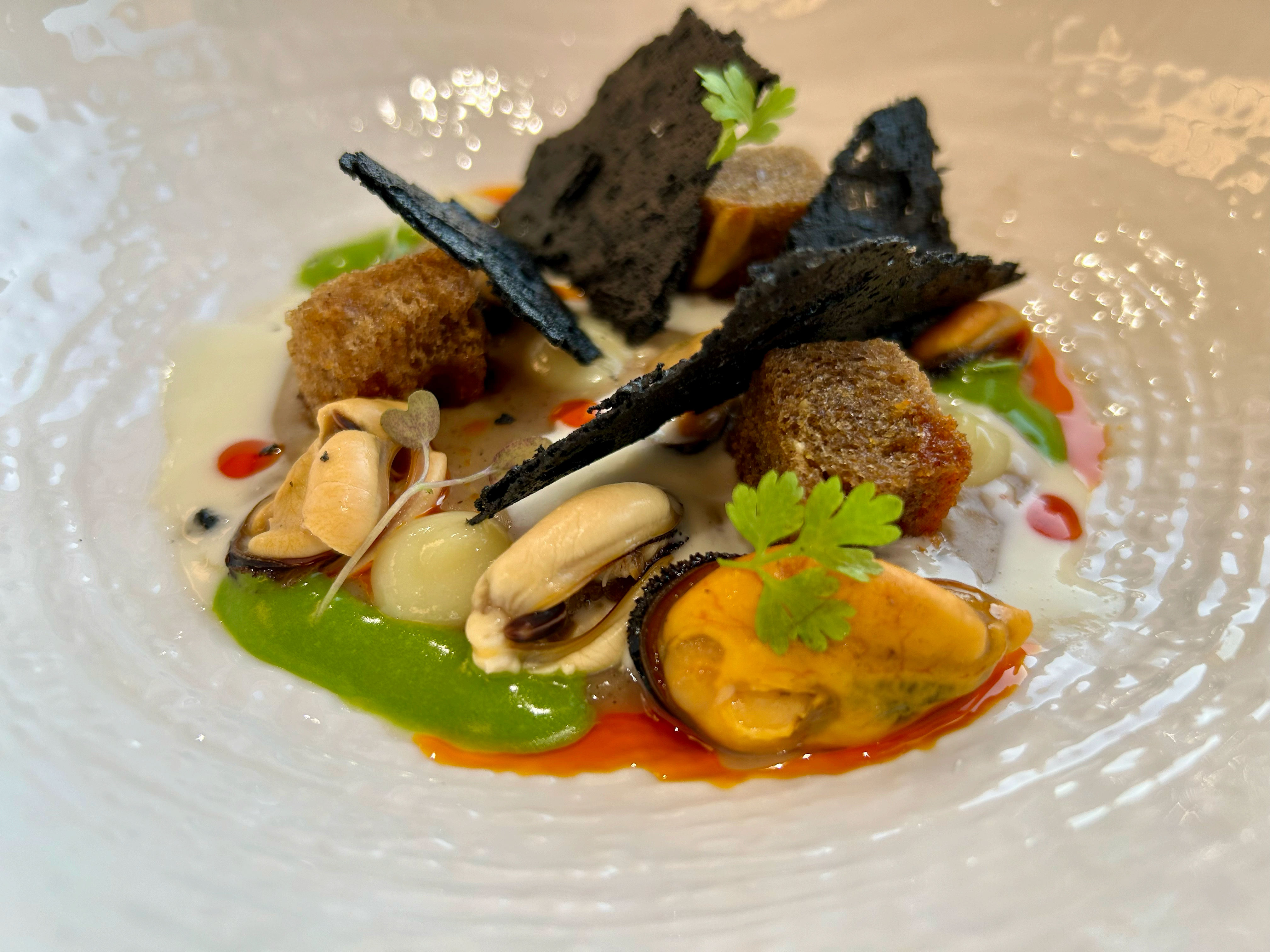 Cozze gratinate scomposte, fonduta di parmigiano, limone salato, gel al prezzemolo e cialda al nero.